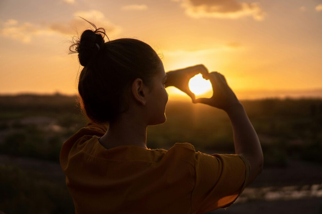 pexels-photo-1535244-1535244 A silhouette of a young woman forming a heart shape at sunset in Kelâat M'Gouna, Morocco.