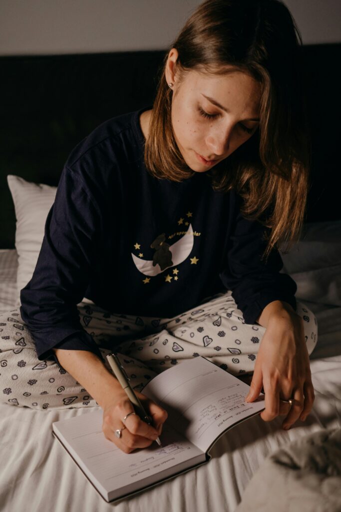 pexels-photo-6541167-6541167 A young woman writing in a journal while sitting on her bed, captured in an intimate and relaxed atmosphere.